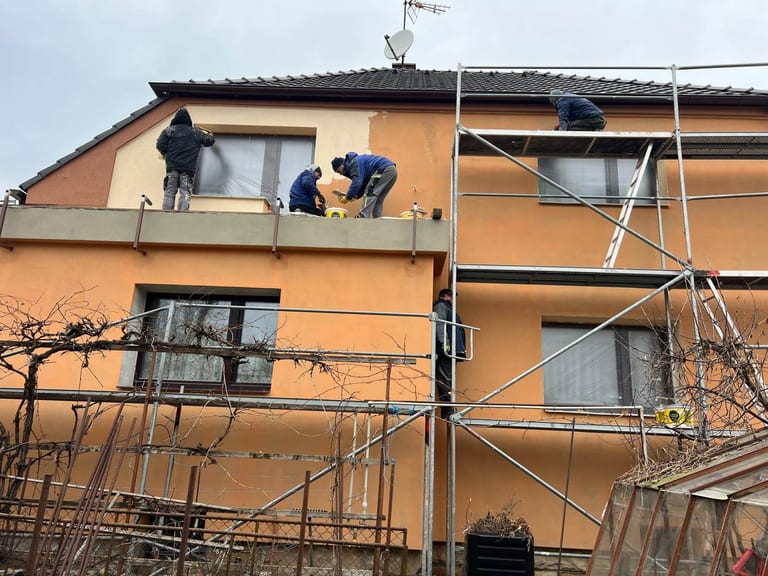 Práce na fasádě rodinného domu s pracovníky na lešení